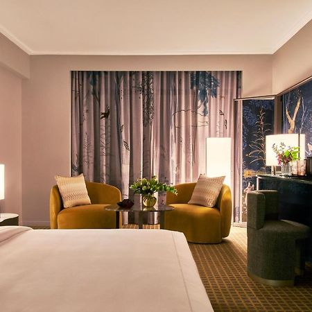 Park Lane New York酒店 外观 照片 The photo shows a stylish hotel room featuring a king-sized bed with a white duvet in the foreground. In the background, there are two contemporary armchairs in a warm yellow color, positioned around a small round table with a floral arrangement. A l