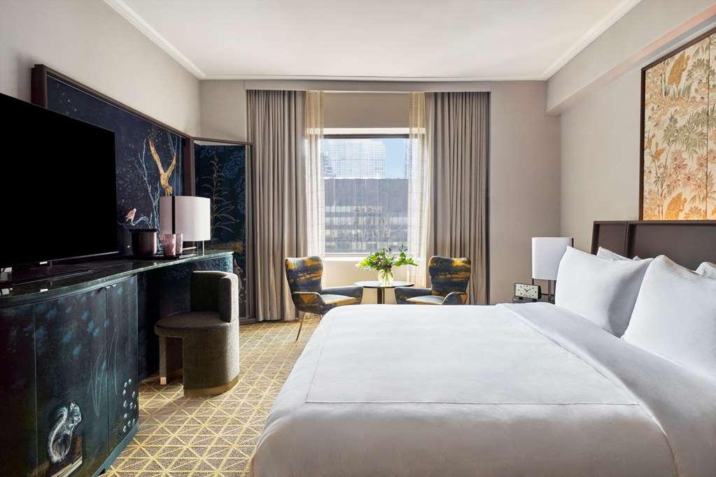 Park Lane New York酒店 客房 照片 The photo shows a stylish hotel room featuring a large bed with white bedding. In the background, there is a large window with curtains that lets in natural light. A small table with two chairs is positioned near the window, suggesting a cozy seating