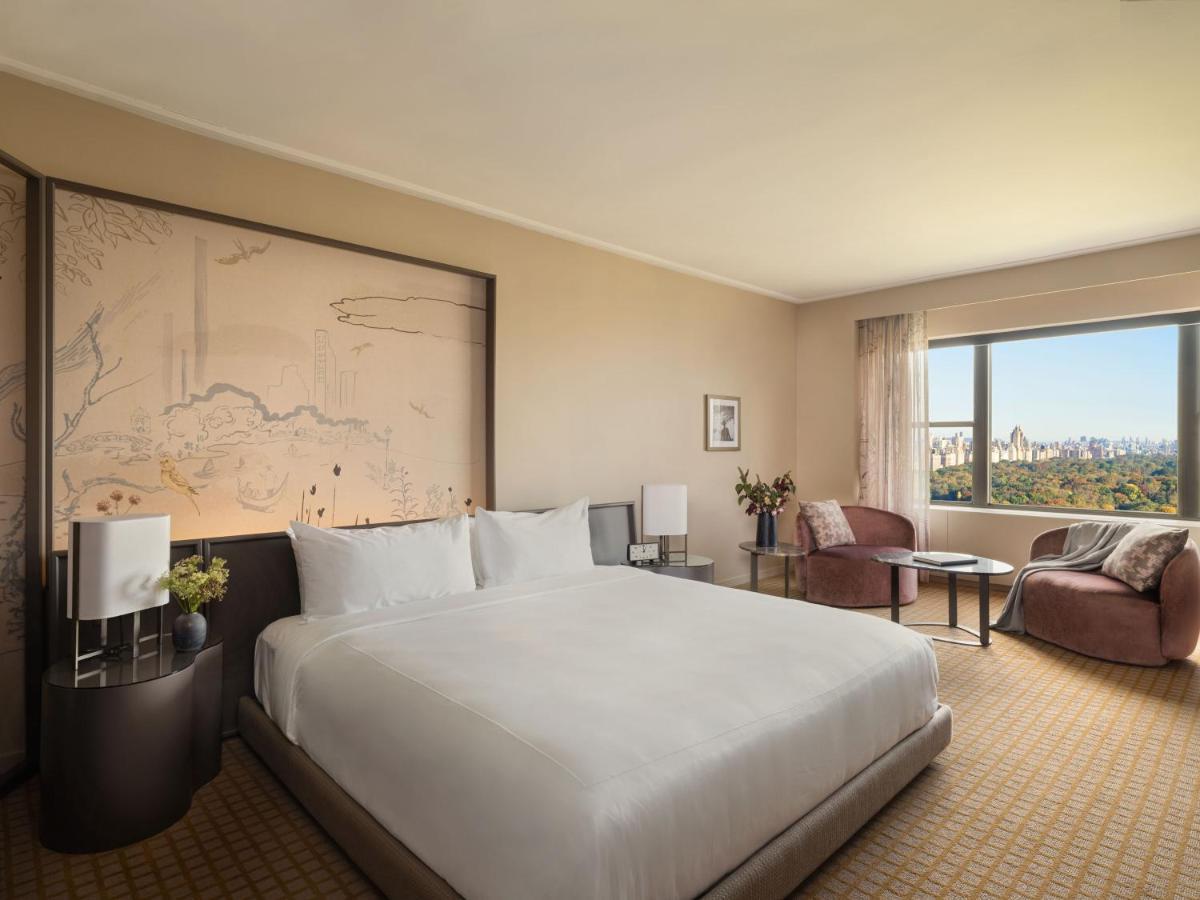 Park Lane New York酒店 外观 照片 The photo shows a modern hotel room featuring a large bed with white linens placed on a stylish platform base. Behind the bed, there is an artistic wall mural, and the decor has a neutral color palette. To the side, there are two comfortable chairs w