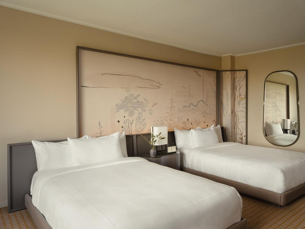 Park Lane New York酒店 外观 照片 The photo shows a modern hotel room featuring two beds with white linens. The background has a large wall art piece that seems to depict a subtle landscape or abstract design. There is a nightstand between the beds with a small decorative item, possi