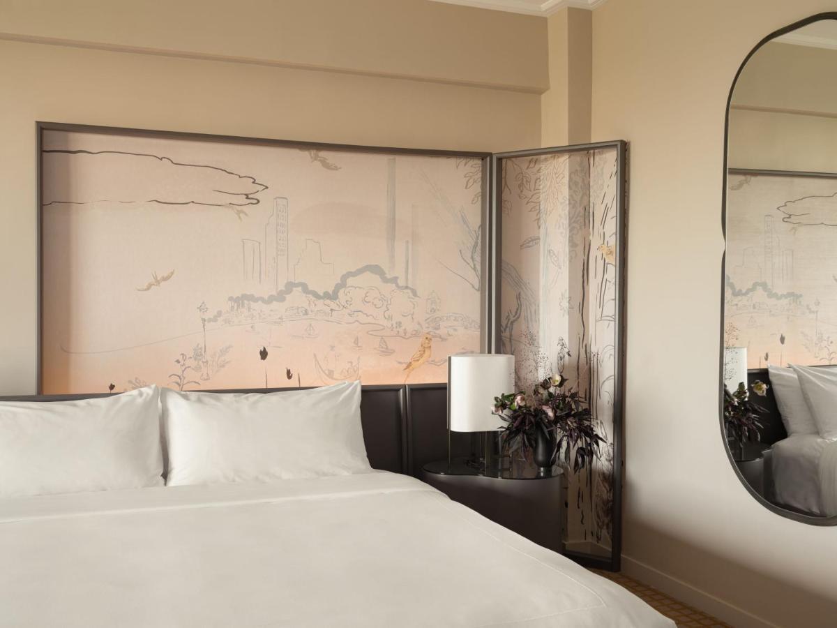 Park Lane New York酒店 外观 照片 The photo shows a modern bedroom featuring a large, neatly made bed with white bedding. Behind the bed is a decorative feature wall illustrated with soft, muted patterns, possibly depicting a landscape or abstract design. To the side, there's a lamp 