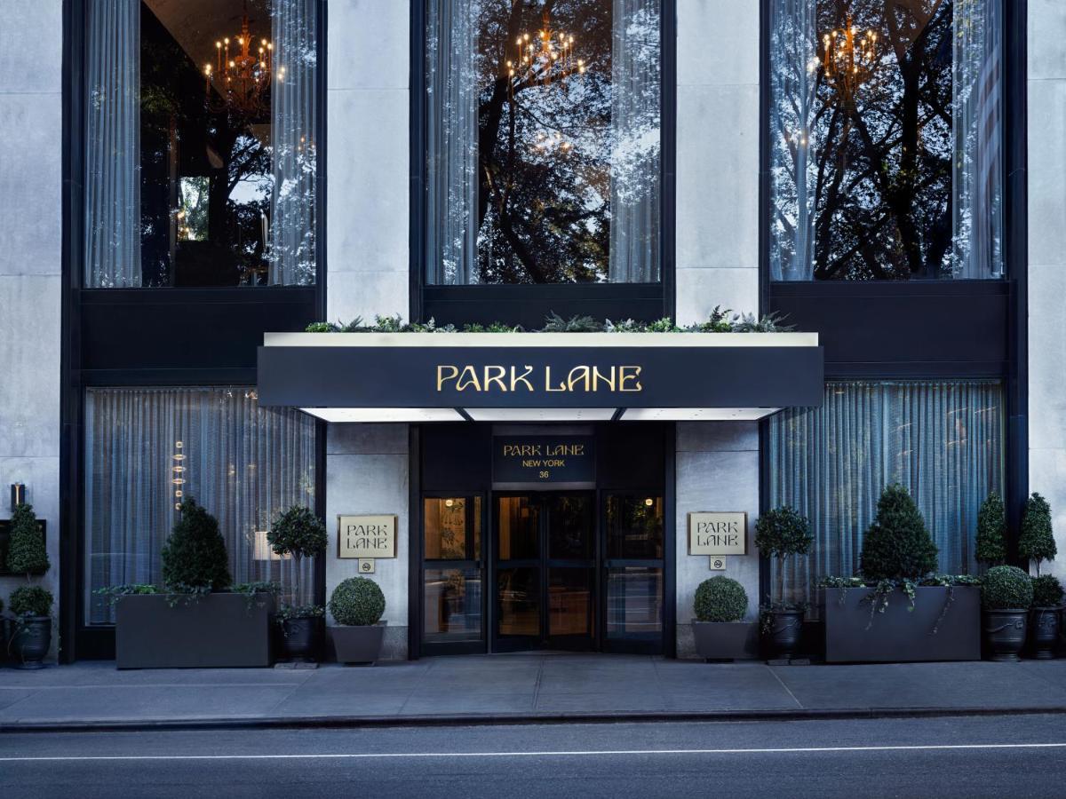 Park Lane New York酒店 外观 照片 The photo shows the entrance of a hotel or building named "Park Lane." The façade features large glass windows, elegant lighting fixtures, and decorative elements like potted plants. The entrance is framed by a dark awning with the name "PARK LANE" p