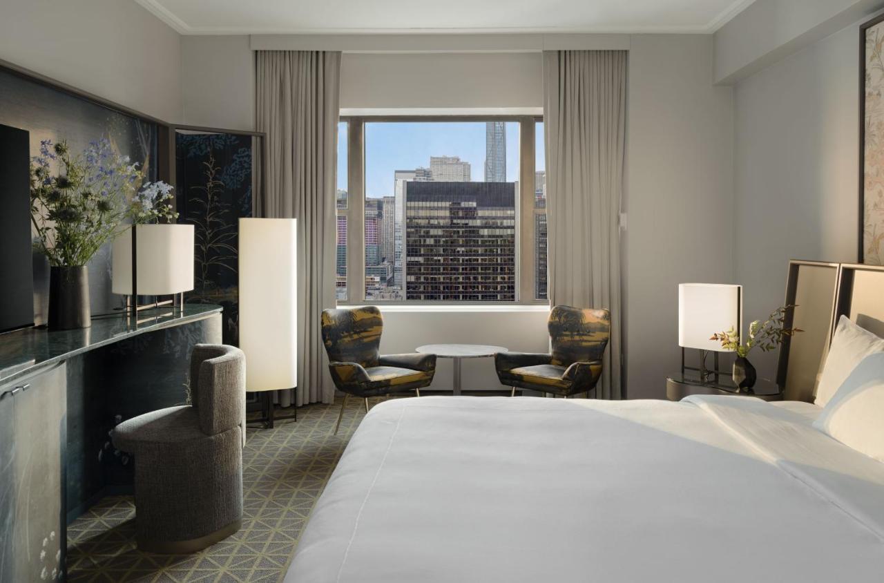 Park Lane New York酒店 外观 照片 The photo shows a stylish hotel room featuring a large bed with white linens. There are two modern armchairs beside a small round table, positioned near a window that offers a view of the cityscape. Natural light flows into the room, highlighting the