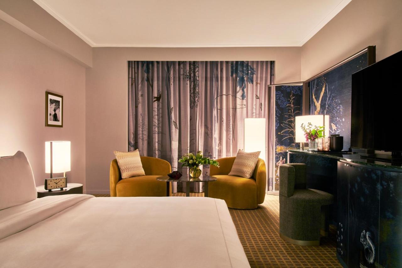 Park Lane New York酒店 外观 照片 The photo shows a stylish hotel room featuring a king-sized bed with a white duvet in the foreground. In the background, there are two contemporary armchairs in a warm yellow color, positioned around a small round table with a floral arrangement. A l