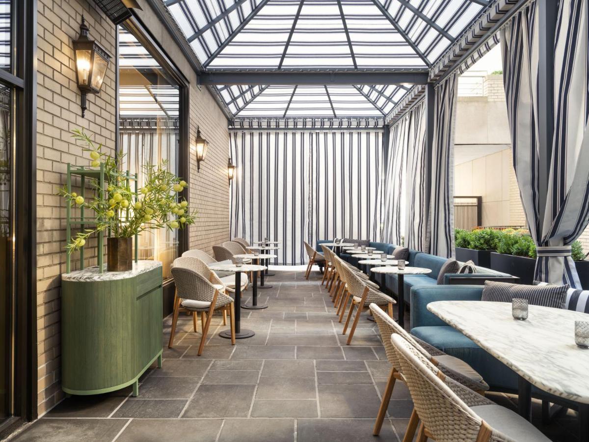 Park Lane New York酒店 外观 照片 The photo shows a stylish indoor dining space, likely a conservatory or a sunroom. The area features a modern design with a glass roof allowing natural light to fill the space. 

The walls are a mix of brick and large windows adorned with striped cur