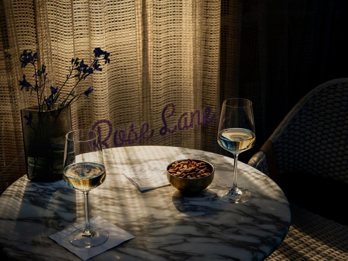 Park Lane New York酒店 外观 照片 The photo shows a cozy setting featuring a marble table with two glasses of white wine. There is a small bowl of nuts on the table, accompanied by two coasters. In the background, a decorative pot contains some flowers, and a textured curtain lets in