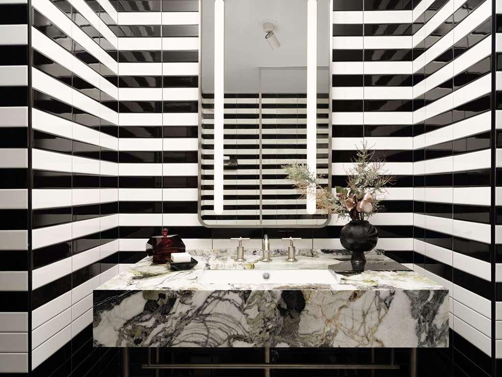 Park Lane New York酒店 客房 照片 The photo shows a modern bathroom with a striking design. The walls are decorated with alternating black and white stripes, creating a bold visual effect. In the center, there is a large, stylish vanity featuring a marble countertop with intricate pa