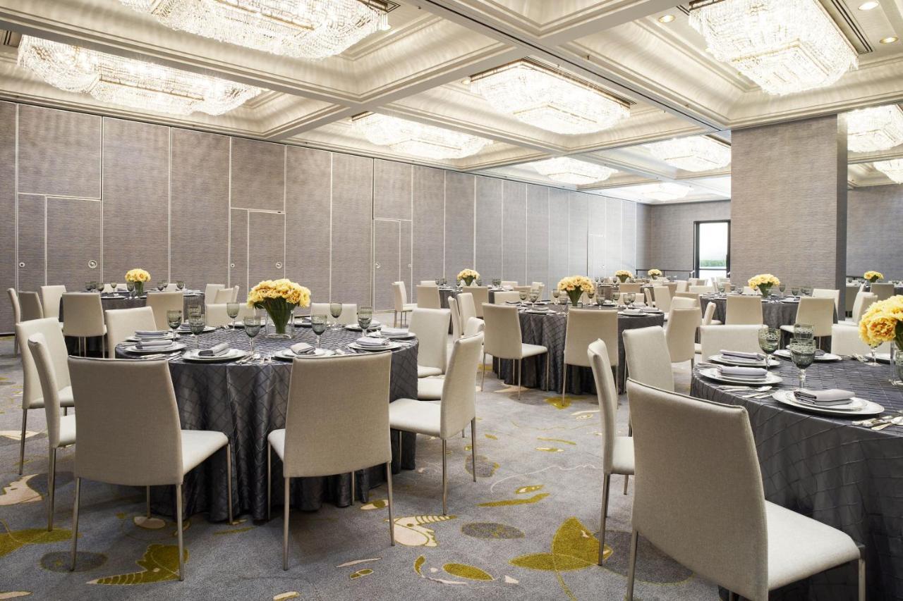 Park Lane New York酒店 外观 照片 The photo depicts an elegant dining or event space. It features several round tables covered with gray tablecloths, each set with plates, glasses, and silverware. Centerpieces of yellow flowers are arranged on most tables. The room has modern, white 