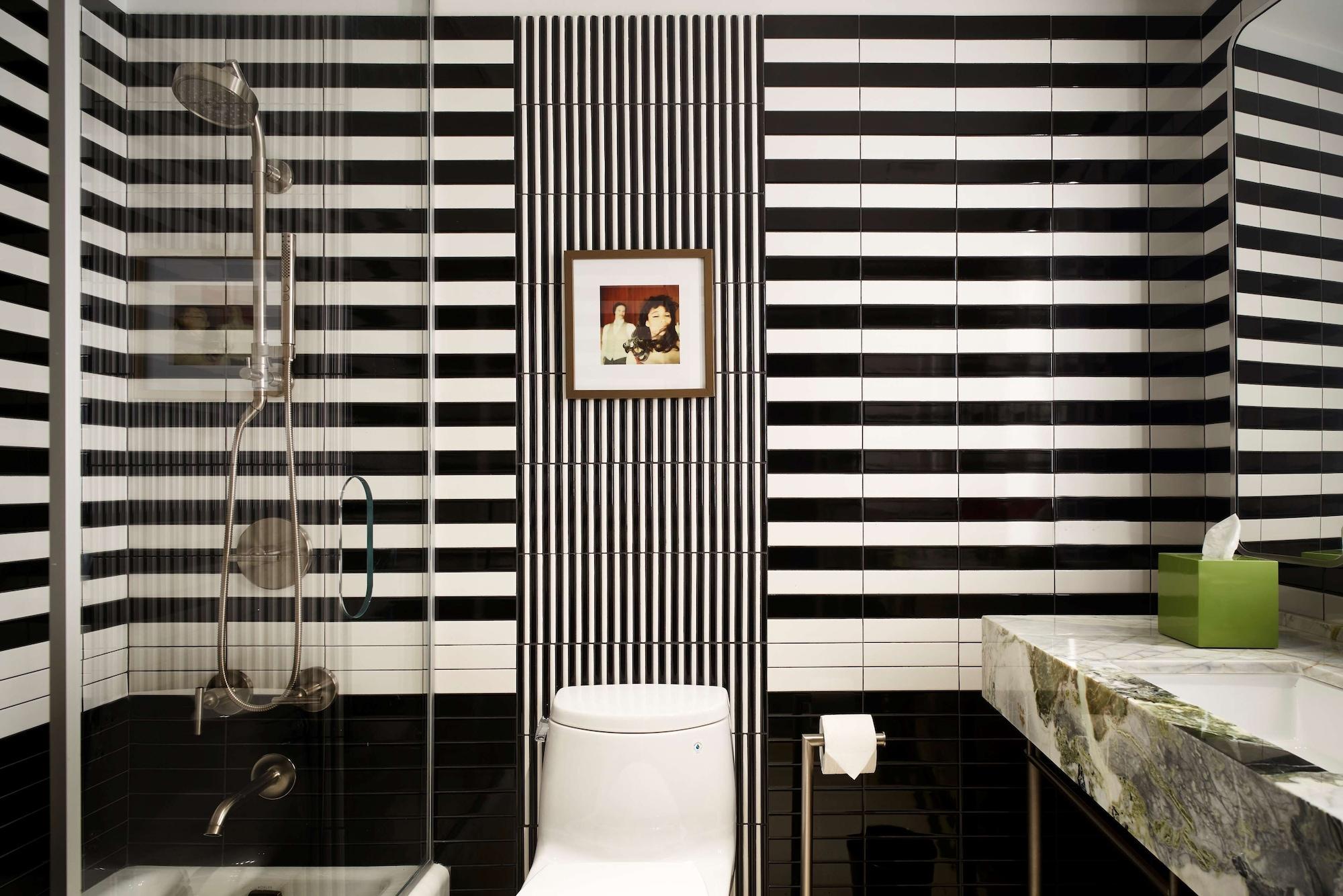 Park Lane New York酒店 外观 照片 The photo shows a modern bathroom featuring a striking design with black and white striped tiles on the walls. There is a glass shower enclosure on one side, and a white toilet sits against the wall. Above the toilet, there is a small framed picture 