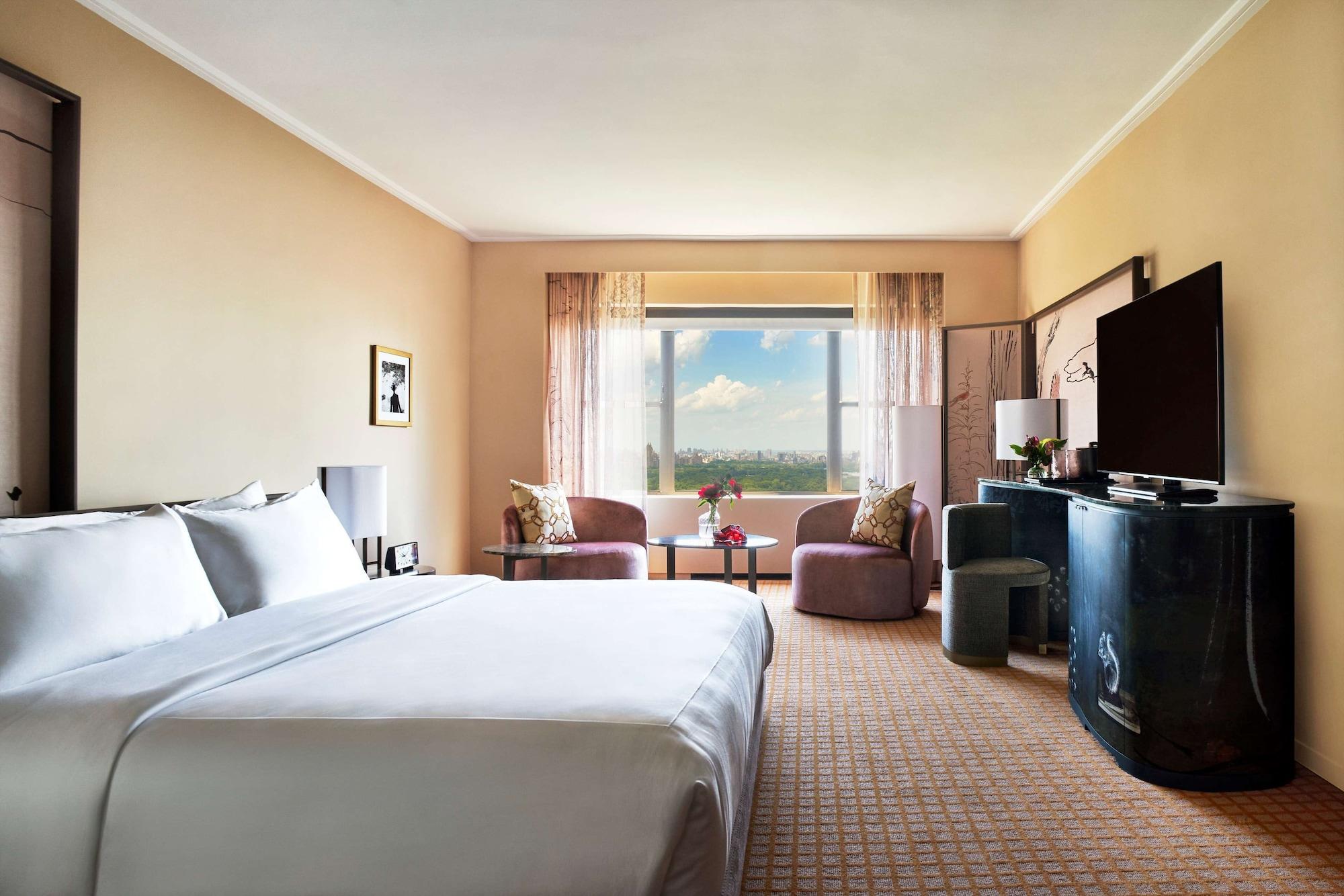 Park Lane New York酒店 外观 照片 The photo shows a spacious hotel room with a warm beige color scheme. There is a large king-sized bed with white linens prominently placed in the foreground. To the side, there are two comfortable-looking chairs facing a small table. 

Across from th