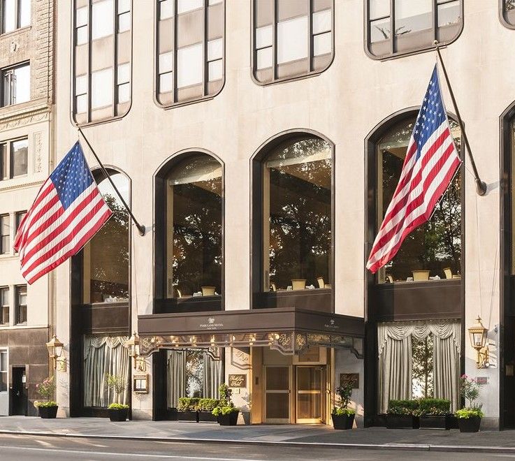 Park Lane New York酒店 外观 照片 The photo shows the exterior of a building, likely a hotel or an upscale establishment. There are two large American flags displayed prominently on either side of the entrance. The entrance features a golden door and decorative elements, while the wi