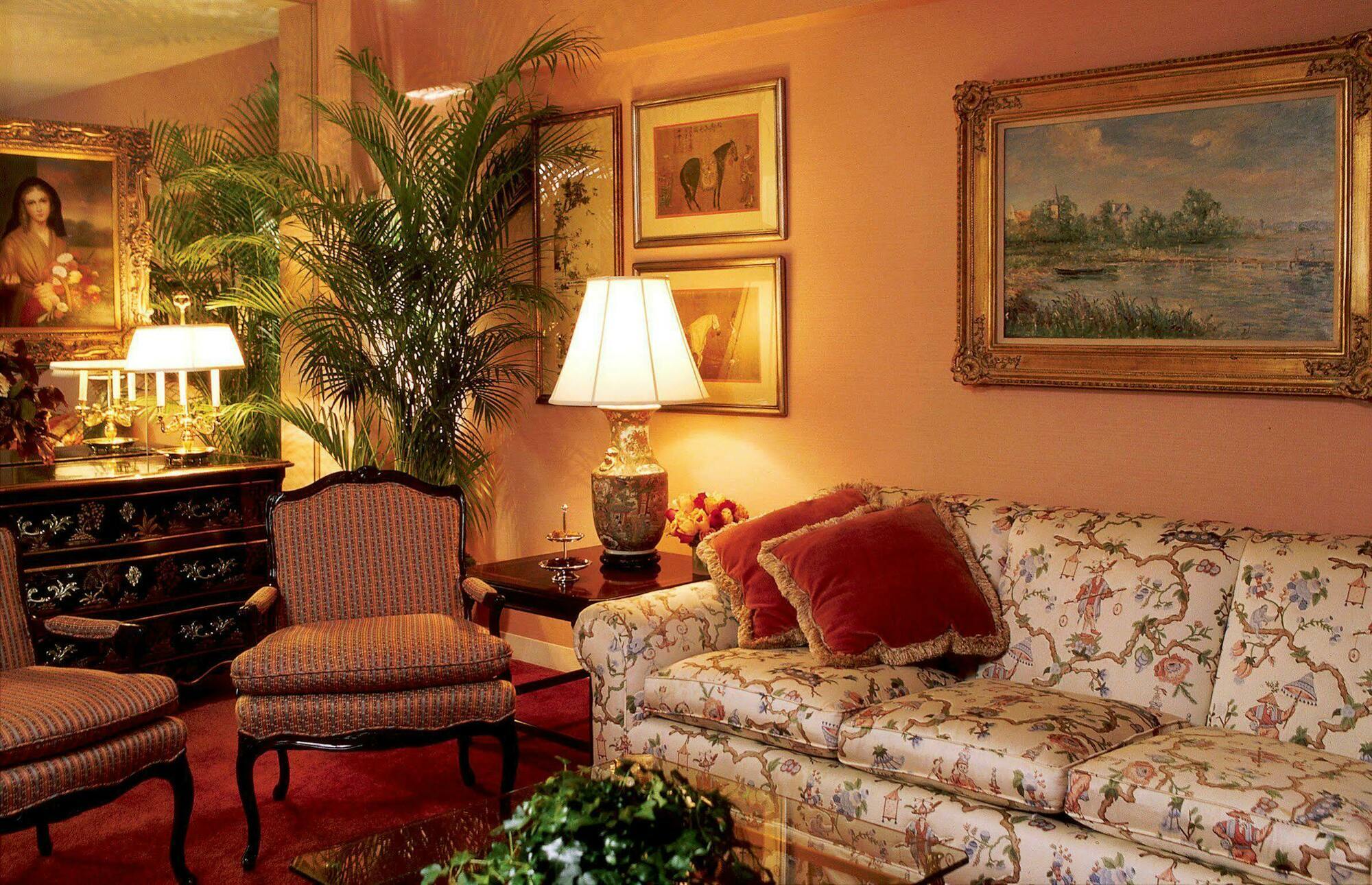 Park Lane New York酒店 客房 照片 The photo shows a cozy living room setting. The walls are painted a warm peach color, and there are several framed paintings hanging on the walls. A floral-patterned sofa with plush cushions is positioned in the room, along with elegant armchairs tha