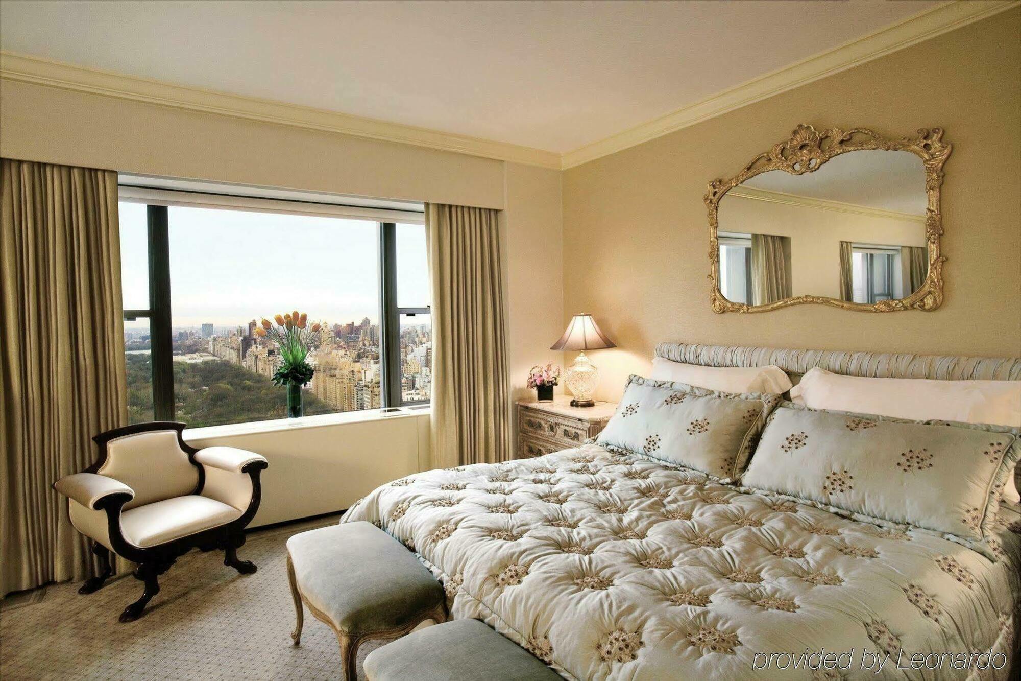 Park Lane New York酒店 客房 照片 The photo depicts a cozy, elegantly decorated bedroom. The focal point is a large bed with a luxurious, tufted comforter featuring floral patterns. To the side of the bed, there's a small upholstered bench. There's a window with stylish drapes, offer