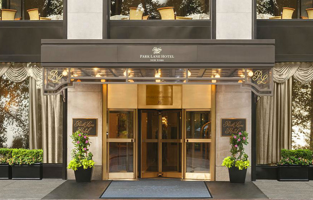 Park Lane New York酒店 外观 照片 The photo shows the entrance of a hotel named the Park Lane Hotel. It features a glass revolving door framed by elegant awning and decorative elements. Flanking the entrance are planters with greenery, and the hotel’s name is displayed prominently ab